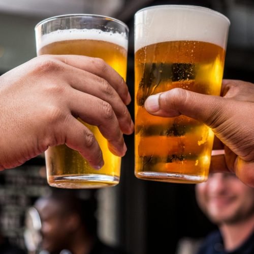Close-up of two friends toasting with cold beer glasses at a lively bar, celebrating friendship and good times.