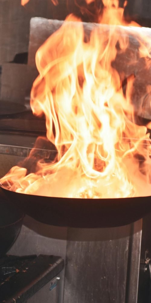 Chef expertly handles flaming pan in a bustling kitchen setting.